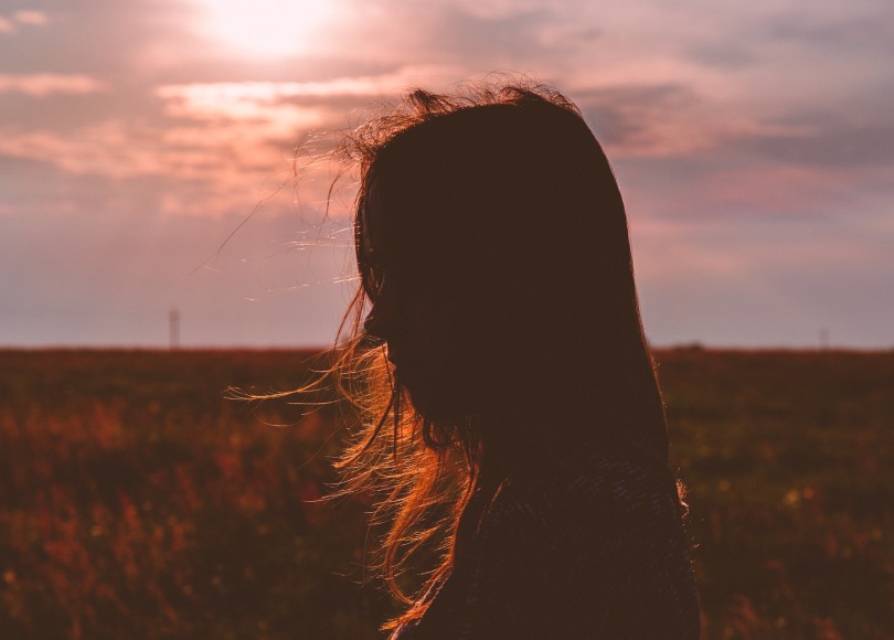 Silhouette of the side of a girls face against a sun set.
