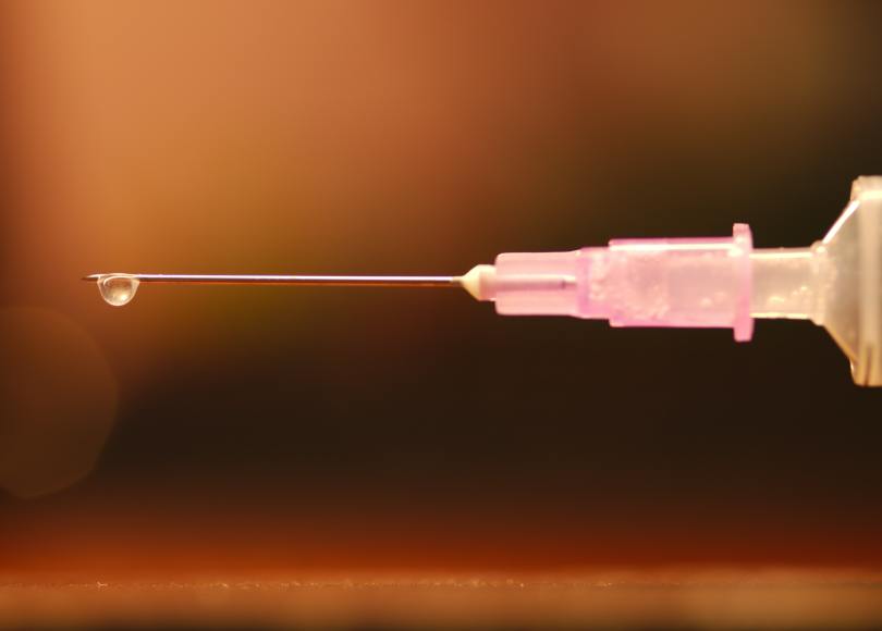 A macro shot of syringe with needle and a drop of liquid suspended from the end