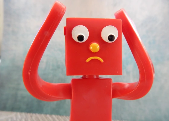 Red robot with square head with his arms up, looking sad and confused.