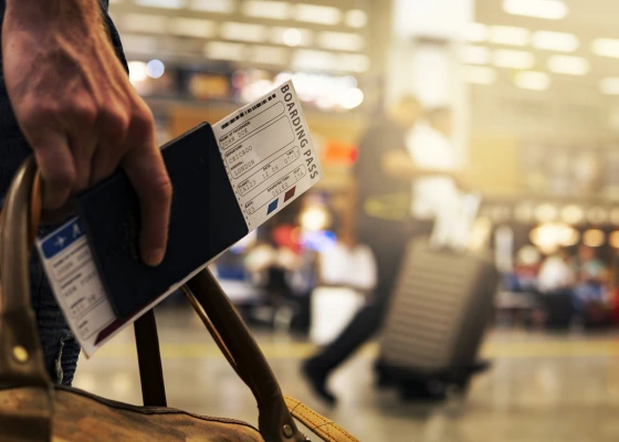 Closeup of a hand holding a flight ticket tucked inside a passport. Blurry background of an airport scene.